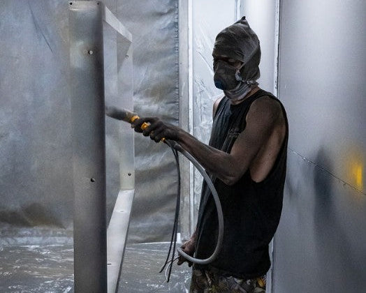 Person powder coating metal in a workshop setting